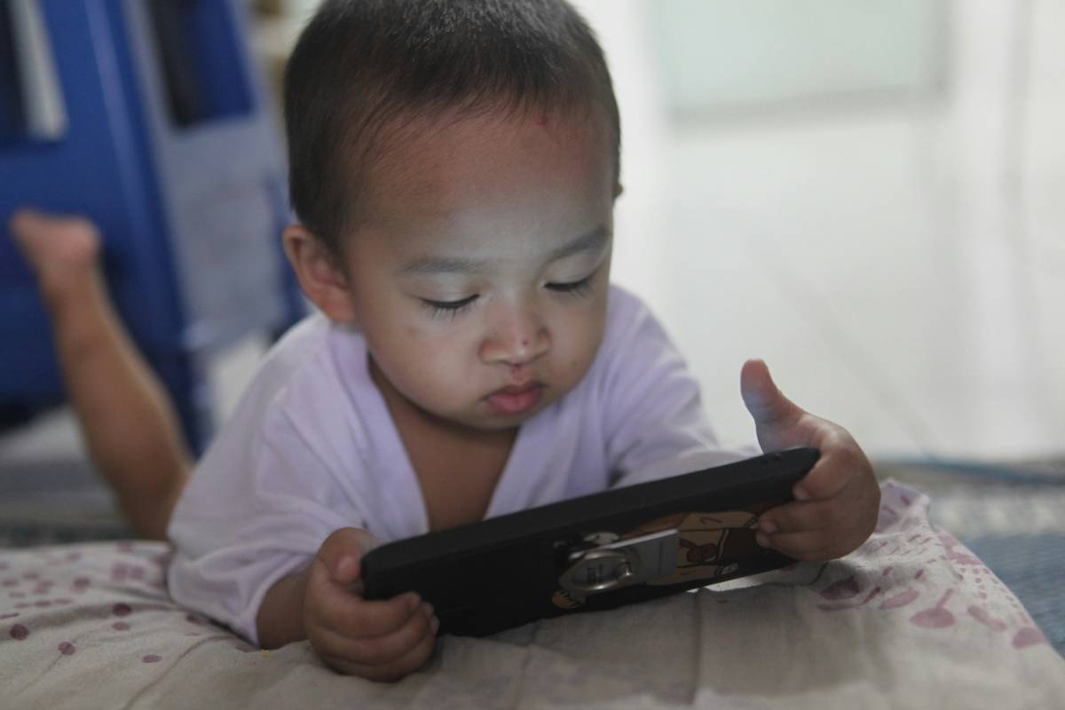 A child playing games on a gaming tablet while parents look concerned in the background